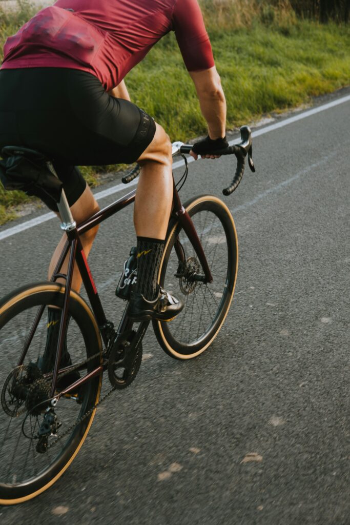 Sportlich gekleideter Radfahrer auf einem sportlichen Fahrrad, aufgenommen in einer Naturumgebung mit Grünflächen im Hintergrund.