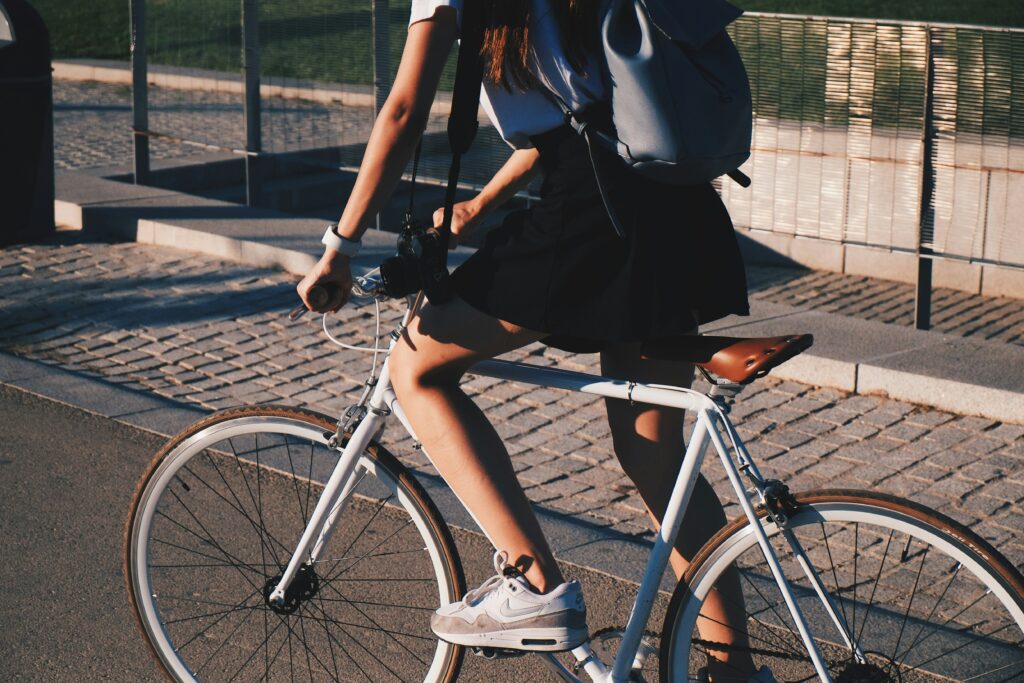 Zu sehen ist eine junge Person in Freizeit-Kleidung und Rucksack auf einem weißen Fahrrad.